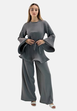 Top gris plisado con mangas acampanadas y un lazo en la cintura, combinado con pantalones anchos gris. La tela tiene una textura sedosa, ofreciendo una silueta fluida.