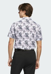 Kurzarmhemd mit geometrischem Muster in Schwarz, Weiß und Grau; leichtes Material; gerade Kragen; getragen mit schwarzen Hosen.
