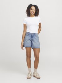Shorts en denim avec un délavage bleu clair, présentant une taille mi-haute, un ourlet effiloché et quatre poches. Assortis à un t-shirt blanc ajusté et des baskets beiges.