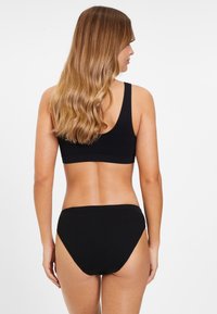 Bralette nera senza cuciture e bikini a vita alta. Tessuto morbido con una texture liscia, caratterizzato da un design minimalista e senza cuciture visibili.