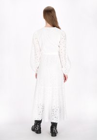 Witte jurk met lange mouwen en broderie anglaise details, met een getailleerde taille, gecombineerd met zwarte kniehoge laarzen met dubbele gespen.