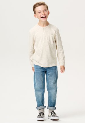 Crème lange mouwen henley shirt met knoopsluiting, lichtblauwe jeans en zwart-witte geblokte sneakers. Casual, relaxed fit met zak.