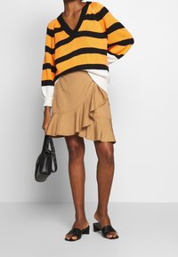 Orange og sort stribet strikket sweater med V-hals; lagdelt over en beige flæset nederdel. Sort håndtaske og sorte slip-on blokhæl-sandaler.