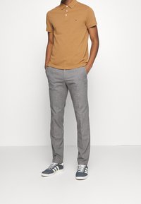Polo shirt tan, pantalon gris, et baskets navy. Le polo est doté d'un col et de trois boutons ; les pantalons sont ajustés avec une finition lisse.