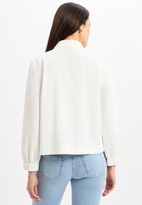 Witte, lichte jack met een kraag, elastische manchetten en een cropped ontwerp. Glad textuur, minimalistische stijl.