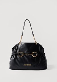 Black leather handbag with gold heart-shaped hardware, a gathered design, and a chain accent on adjustable straps. Logo displayed on front.