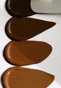 Fire stykker malingsprøver i varierende nyanser av brunt, blank overflate, hver i dråpeform, ordnet på en hvit bakgrunn.