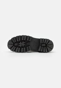 Suela de zapato de goma negra con un patrón de banda de rodadura profundo, que presenta ranuras y crestas para una mejor tracción; incluye un logotipo de marca visible.