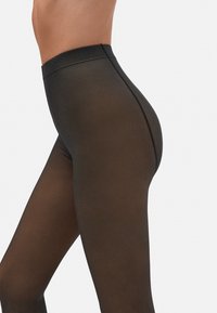 Leggings negros de cintura alta hechos de un material suave y semitranslúcido, con un ajuste ceñido y costuras sutiles a lo largo de los lados que realzan la forma.