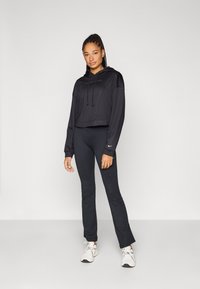 Black cropped hoodie with adjustable drawstrings, partnered with black fitted leggings and light sneakers, featuring logo accents on both.