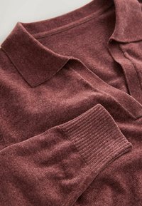 Burgundy knitted pullover with a polo collar, featuring a textured yarn and ribbed cuffs. Soft, medium-weight fabric with a subtle sheen.
