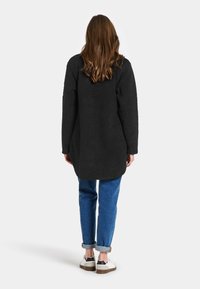 Sort, fluffy langærmet frakke med en afslappet pasform, der har en rund kant og er under hoften i længden, kombineret med blå jeans med opnåede ærmer og hvide sko.