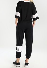 Zwarte sportoutfit met een losse zwarte shirt met witte mesh-strepen en bijpassende zwarte broek met witte manchetten en logo-detail.