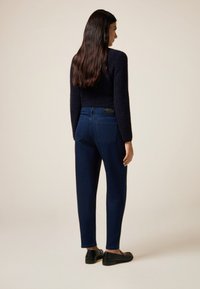 Maglione aderente blu navy con maniche lunghe, abbinato a jeans in denim scuro di vestibilità comoda, dotati di tasche posteriori e mocassini neri.