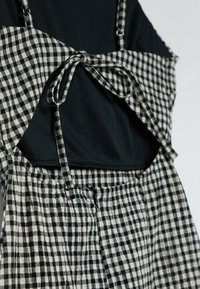 Sort-hvidt gingham-mønstret kjole med justerbare stropper, der har en knyttet front og et ensfarvet sort indre lag. Tekstureret stof.
