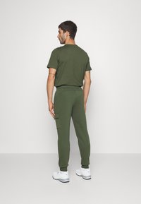 Camiseta de algodón verde oliva y pantalones de chándal a juego con bolsillos tipo cargo, puños de canalé y un corte relajado. Llevado con zapatillas blancas.