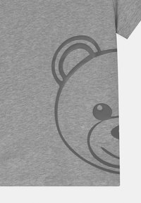 Šedé tričko s krátkým rukávem s grafickým potiskem tmavě šedé medvědí tváře na přední straně, s hladkou texturou a ležérním designem.