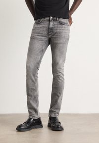 Jeans ajustados grises de denim, con detalles de desvanecimiento, estilo clásico de cinco bolsillos y talle medio, combinados con zapatos negros.