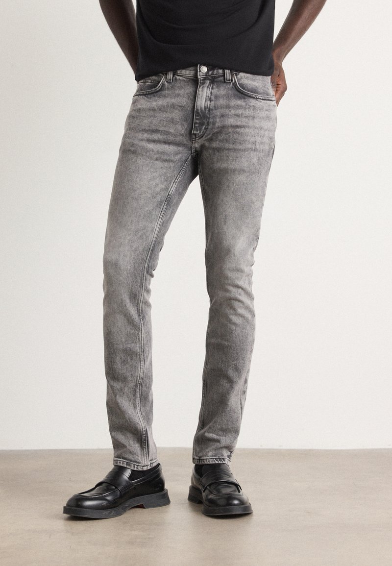 Jeans ajustados grises de denim, con detalles de desvanecimiento, estilo clásico de cinco bolsillos y talle medio, combinados con zapatos negros.