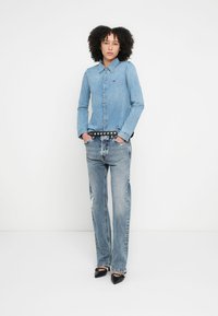 Svetlomodrá denimová košeľa s gombíkmi a špicatým golierom, kombinovaná so svetlomodrými džínsami s ošúchaným efektom a čiernym opaskom so cvokmi. Čierne lodičky.