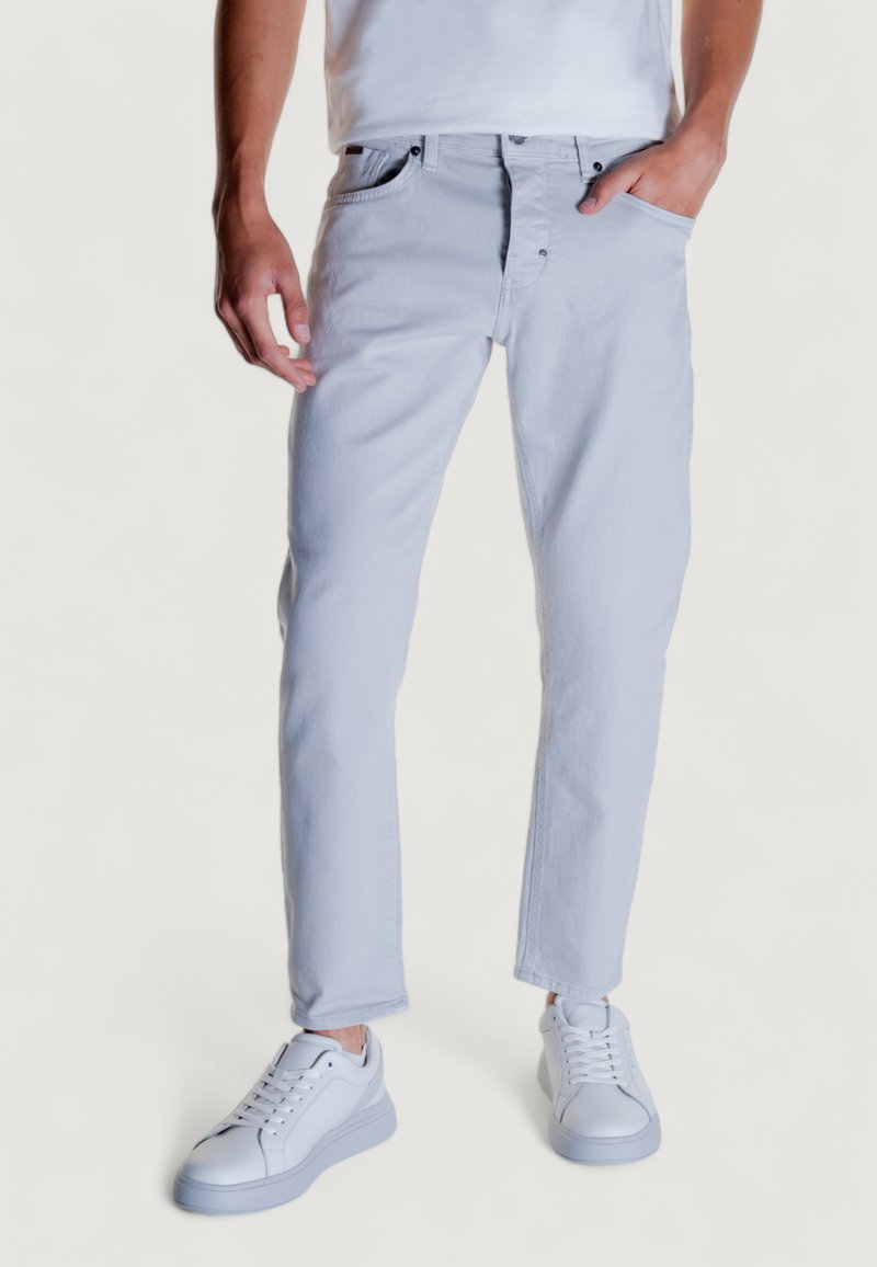Jeans de mezclilla gris claro con un corte ajustado, diseño de cinco bolsillos y cierre con cremallera. Combinados con zapatillas blancas, con cordones planos.