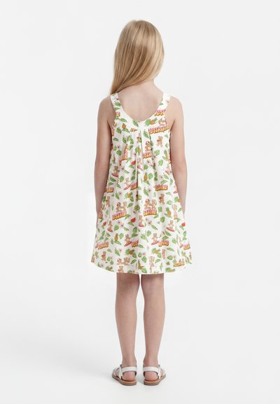 Παιδί με μακριά ξανθά μαλλιά που φοράει αμάνικο λευκό φόρεμα με πολύχρωμα σχέδια από αρκουδάκια και τροπικά φύλλα, στέκεται γυρισμένο προς τα πίσω με άσπρα σανδάλια.