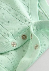 Ljus mintgrön bodysuit med texturerad stickad mönster, som har metalliska tryckknappar i botten och mjuka ribbade hals- och ärmhål.