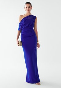 Karaliskā zila vakarkleita ar vienu plecu, ar krokotu faktūru, pieguļošu siluetu un plūstošu audumu. Aksesuārs - bēša rokassoma.