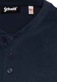 Maglietta henley blu scuro realizzata in tessuto morbido, con patta dei bottoni, colletto a coste e taschino sulla sinistra. Etichetta del marchio visibile.