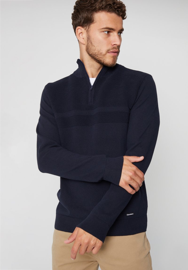 Dunkelblauer Pullover mit einem halben Reißverschluss am Kragen, gerippter Textur und horizontalen Streifen auf der Brust, mit gestrickten Bündchen und Saum.