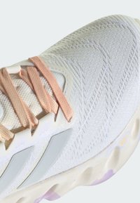 Scarpa da running leggera in mesh bianco, con lacci pesca e accenti grigi, dotata di una tomaia testurizzata e di una suola multicolore ben imbottita.