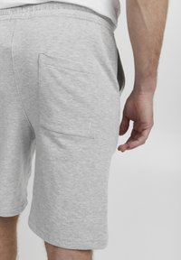 Pantaloni scurți gri din bumbac, cu un tiv elastic, o buzunar pe spate și o croială dreaptă, având textură vizibilă și detalii de cusătură.