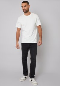 Weißes Baumwoll-T-Shirt mit rundem Ausschnitt, kombiniert mit schwarzen, eng anliegenden Jeans und weißen Sneakers mit schwarzen Akzenten. Glatte Textur, lässiges Design.