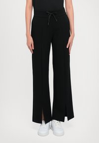 Zwarte wijde broek met een trekkoord in de taille, met zijslits. Gemaakt van een soepele stof, gecombineerd met witte sneakers.