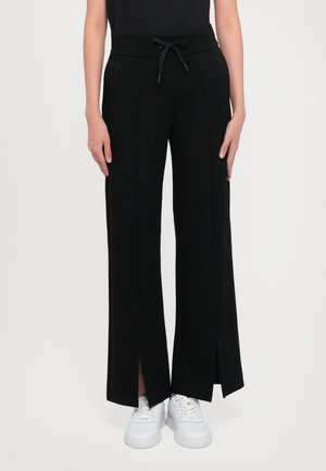 Zwarte wijde broek met een trekkoord in de taille, met zijslits. Gemaakt van een soepele stof, gecombineerd met witte sneakers.