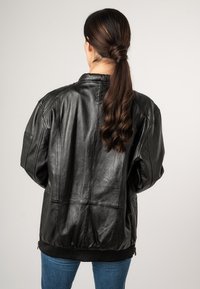 Zwarte leren jas met een comfortabele pasvorm, voorzien van een geribde zoom en manchetten, zichtbare naaddetails en een soepele textuur.