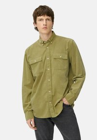 Olive green button-up shirt made of soft fabric, with two chest pockets, long sleeves, and a classic collar, paired with dark jeans.