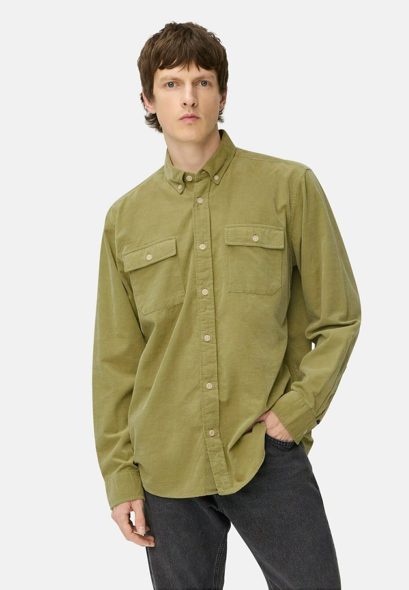 Olive green button-up shirt made of soft fabric, with two chest pockets, long sleeves, and a classic collar, paired with dark jeans.