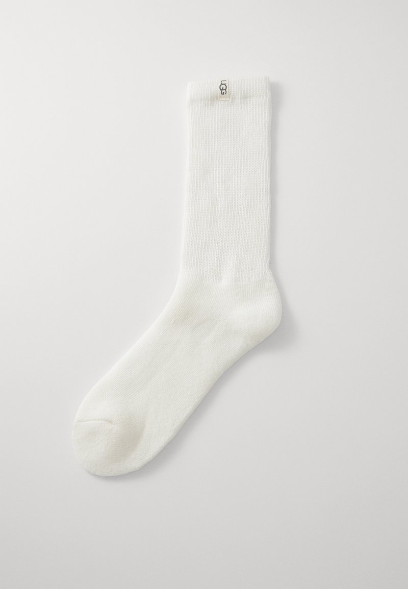 Hvite sokker til midten av leggen med ribbet tekstur og UGG-logo på toppen, mot en enkel lys bakgrunn.