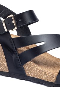Sandaletta nera in pelle con zeppa, presenta una soletta in sughero, una fascia regolabile con fibbia metallica e suola nera texture.