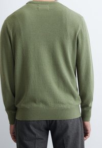 Groene gebreide trui met een gladde textuur, ronde halslijn en ribgebreide manchetten, gecombineerd met grijze gestructureerde broek.