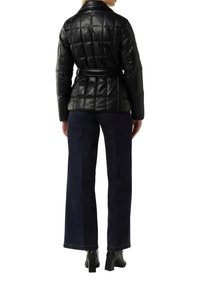 Schwarze gesteppte Lederjacke mit tailliertem Bund, ausgestattet mit einem Kragen und einem strukturierten Muster, kombiniert mit lässigen weit geschnittenen dunklen Denim-Hosen und Stiefeletten mit Absätzen.