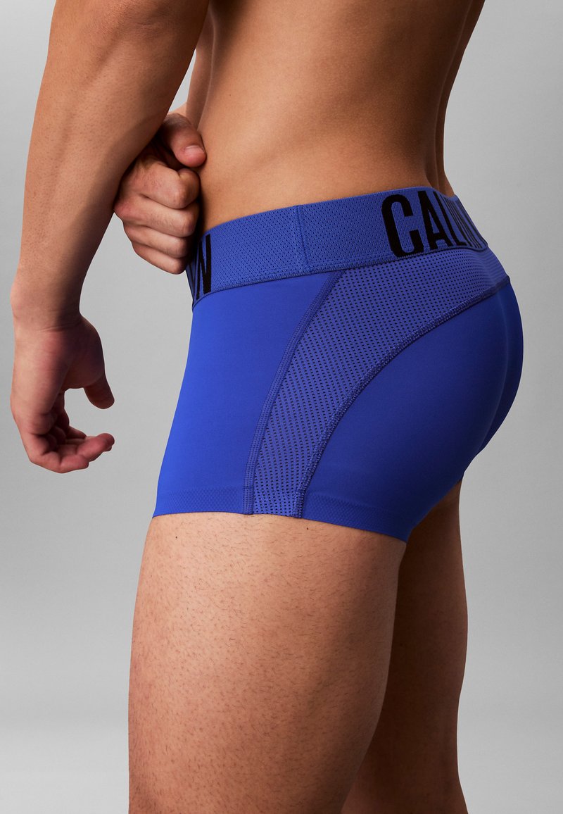 Blauwe boxershorts van rekbare stof. Heeft een gestructureerd zijpaneel en een tailleband met een logo in contrasterend zwart.