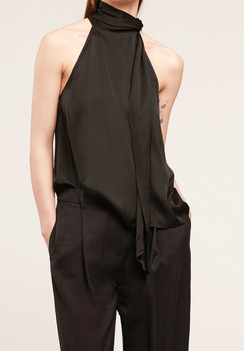 Haut noir à col licou avec un détail noué au niveau du cou, en tissu lisse. Associé à un pantalon noir taille haute avec poches latérales.