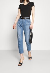 T-shirt noir à col en V, jeans bleu clair taille haute, ceinture noire et mules à talons noires ; portant un petit sac à main noir.