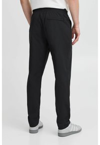Pantalones negros con una cinturilla elástica y un bolsillo trasero, hechos de una tela suave. Diseño de pierna recta, llevados con zapatillas deportivas grises.