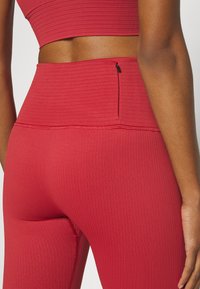 Leggings da allenamento rossi a coste con vita alta e una piccola tasca con zip. Il tessuto ha una finitura strutturata e un design aderente.