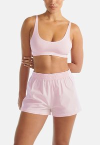 Jasnoróżowy stanik sportowy z okrągłym dekoltem i cienkimi ramiączkami, zestawiony z pasującymi jasnoróżowymi szortami z elastycznym pasem i bocznymi paskami.
