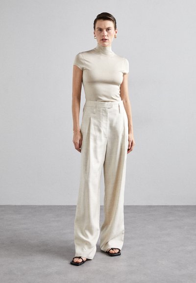 Μπεζ εφαρμοστή μπλούζα με ψηλό λαιμό που συνδυάζεται με ανοιχτό μπεζ παντελόνι με φαρδιά καμπάνα. Υφασμάτινη υφή με κομψό φινίρισμα και ελάχιστες λεπτομέρειες.
