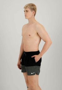 Costume da bagno Nike neri e grigi con vita regolabile, tasche laterali e un logo sulla gamba sinistra. Tessuto liscio con un taglio moderno.